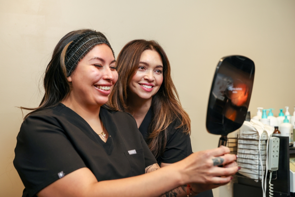 MedSpa nurse injector consulting with client using a handheld mirror, reflecting trust, expertise, and natural aesthetic outcomes.