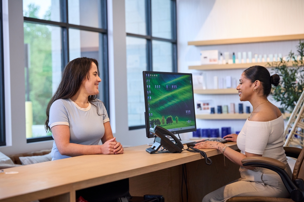 MedSpa front desk staff warmly welcoming a client during check-in, highlighting personalized service and a professional, modern aesthetic clinic environment.