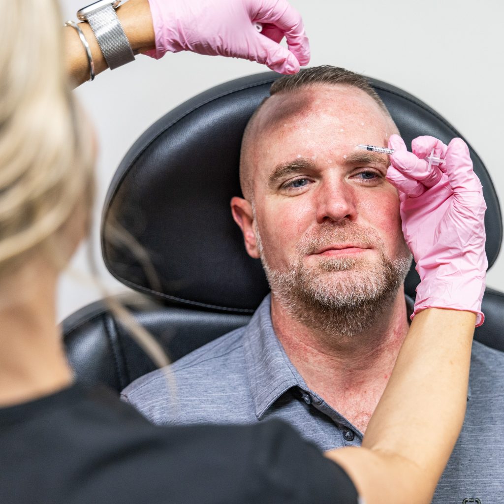 MedSpa provider in pink gloves administering a Botox injection to a middle-aged male client’s forehead during a wrinkle-reduction treatment.