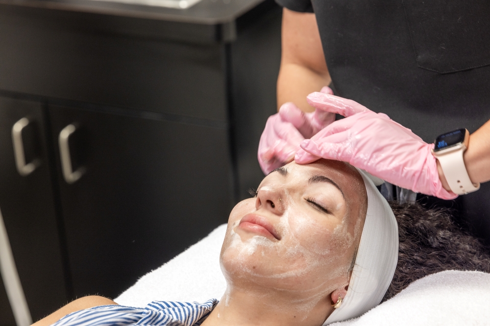 Close-up of MedSpa client receiving a facial, with a provider in pink gloves applying a cleanser to the client's forehead in a calm, clinical environment.
